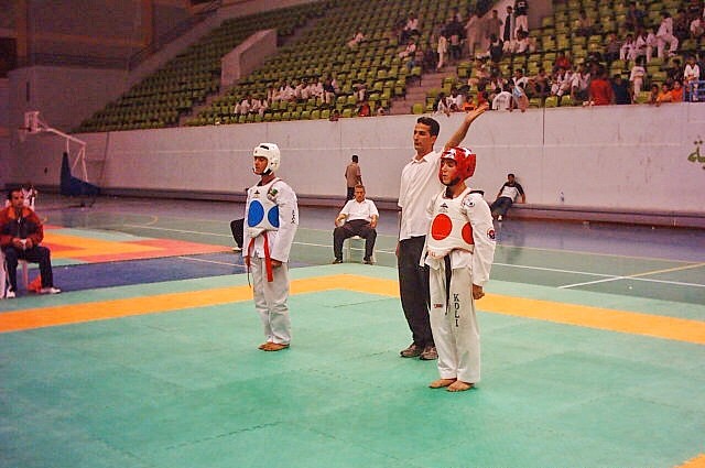 A taekwondo referee raising a hand between two young competitors
